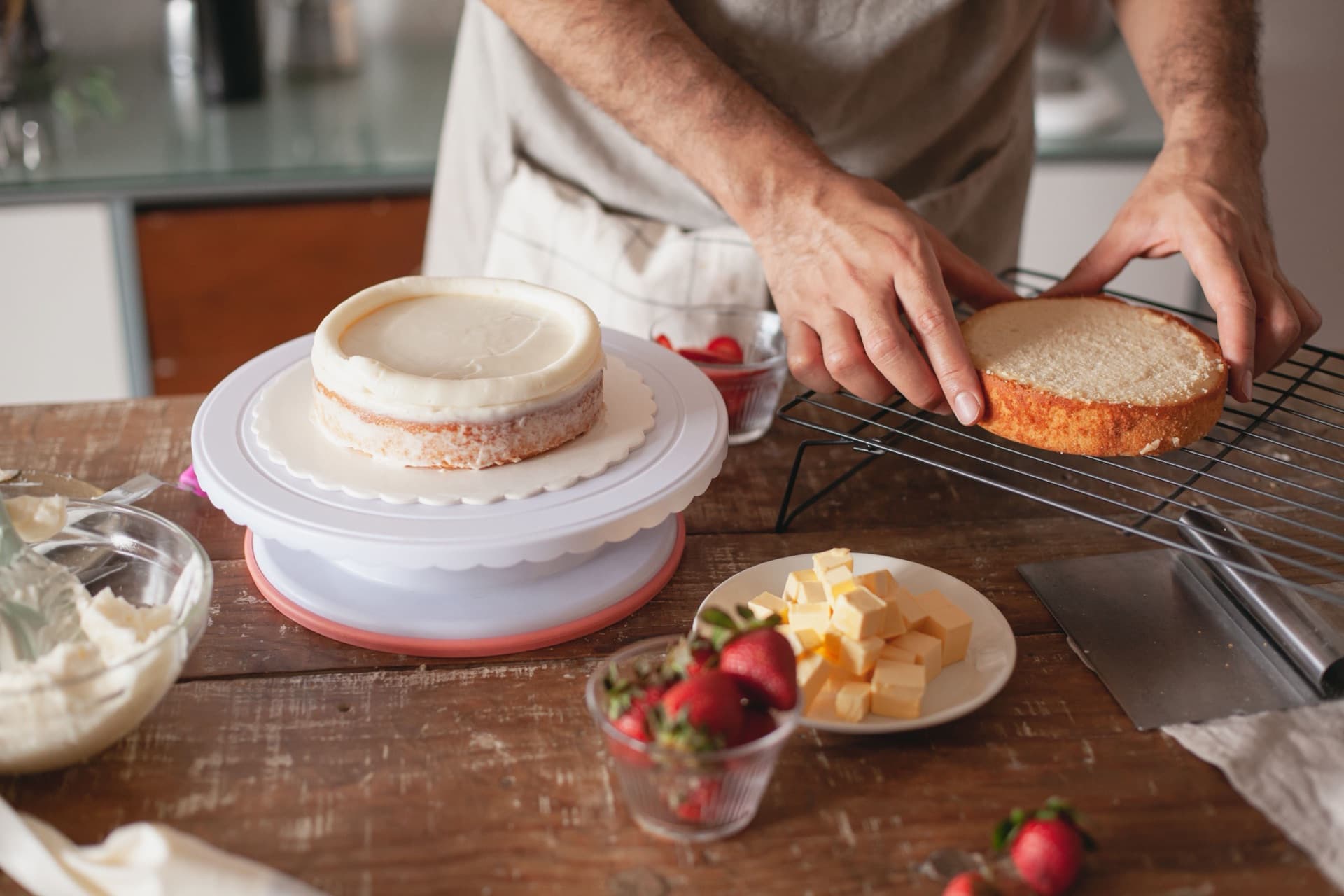 A cake being assembled on a work surface, with cream, strawberries and butter alongside